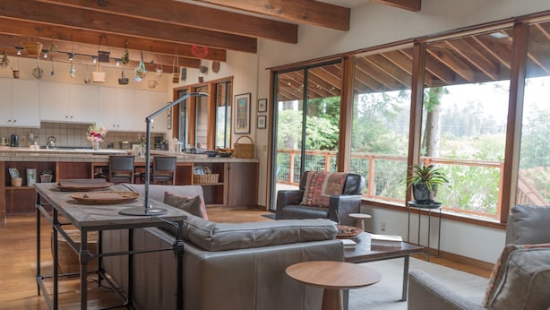 A modern kitchen with wooden beams, a dining area with a sofa and table, and large windows offering a view of greenery. - Family Friendly Home on 20 Acre Farm (Caspar)