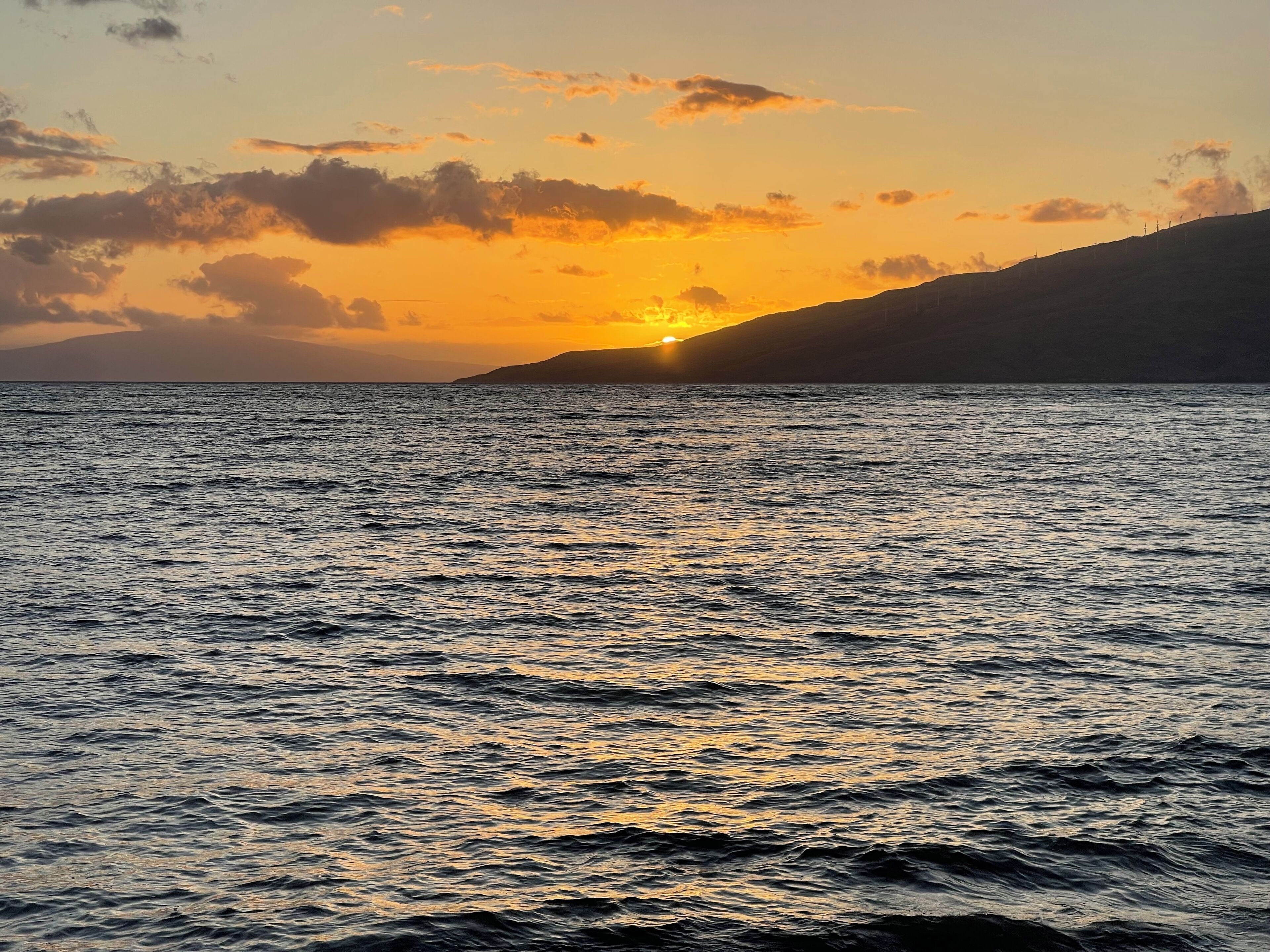 Ein Sonnenuntergang über einem ruhigen Meer mit verschwommenen Landformen im Hintergrund.