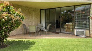 Een tweelaags gebouw met een overdekte patio, compleet met een tafel en stoelen, een kleine tuin en een schuifdeur naar de binnenruimte.