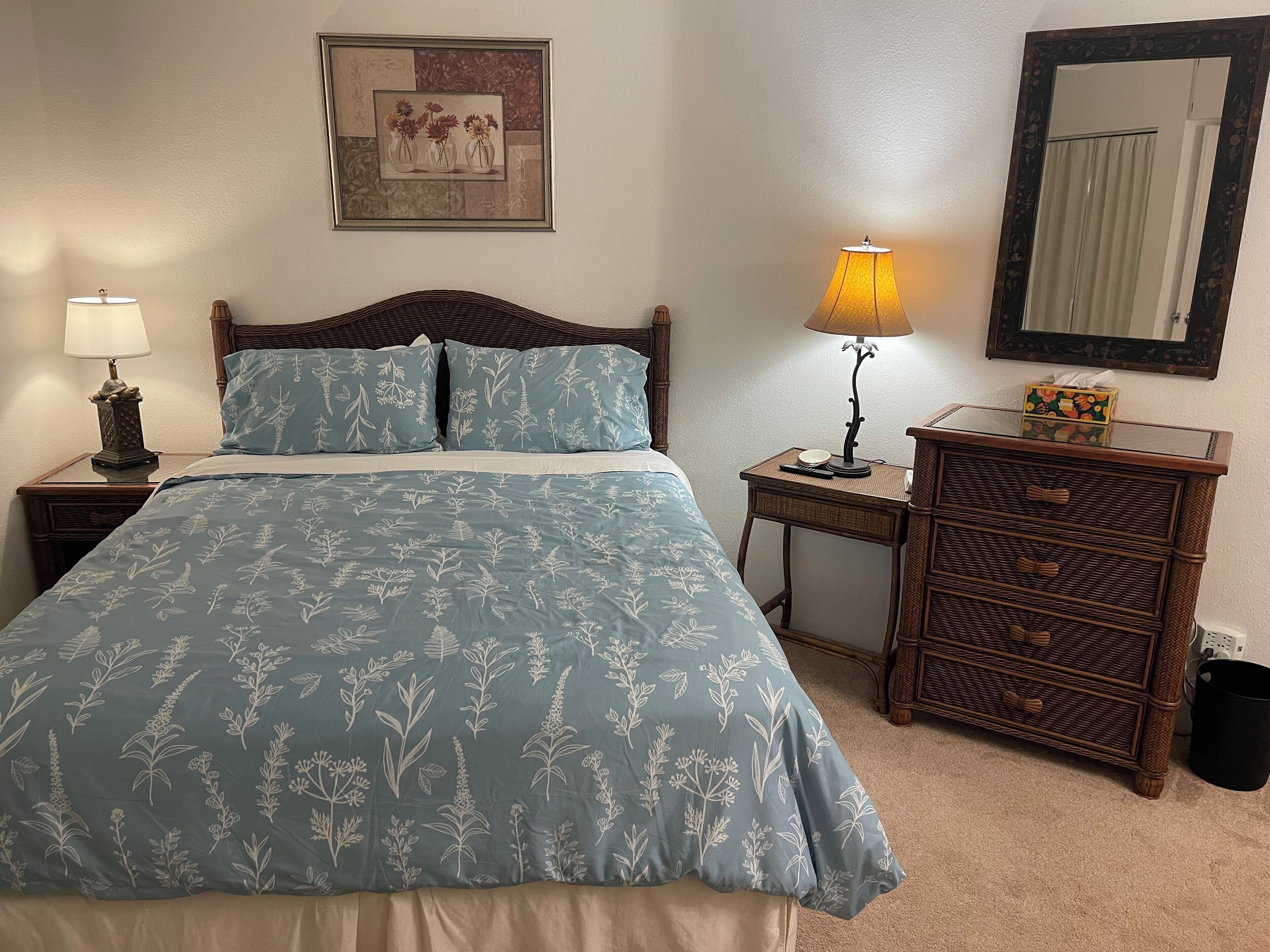 Une chambre à coucher comprenant un lit, une table de chevet, une commode, une lampe, un miroir et un tableau encadré accroché au mur.
