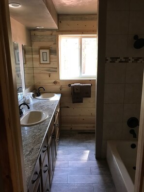 Een houten badkamer in een chalet, met een wastafel, spiegel en raam.