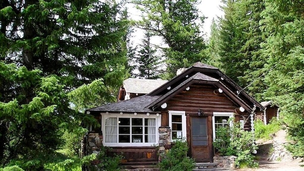 A rustic log cabin with a stone foundation, a wooden door, and a window with a 'OPEN' sign.