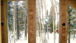 A cabin with three large windows offering views of a snowy forest.