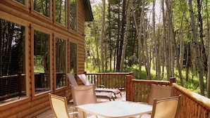 A wooden deck with a table and chairs, surrounded by tall trees.