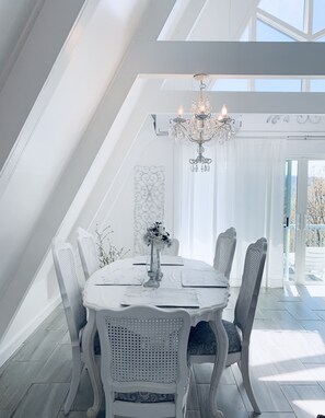 A dining area with a white table set for four, a chandelier, and a view of the outdoors. - Beautiful Mountain Home with Gorgeous View (Franklin)