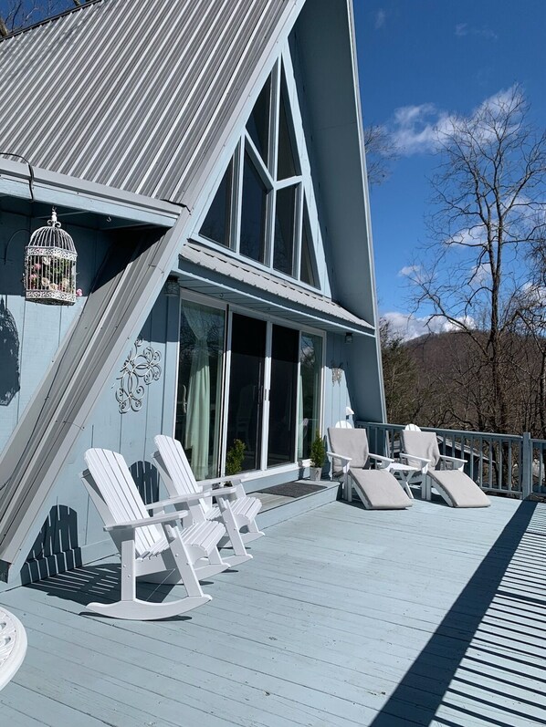 A modern house with a sloped roof, large windows, and a deck with white Adirondack chairs. - Beautiful Mountain Home with Gorgeous View (Franklin)