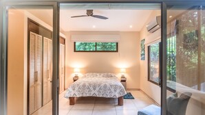 Une chambre à coucher avec un lit, des lampes de chevet, un ventilateur de plafond et une fenêtre donnant sur un paysage verdoyant.