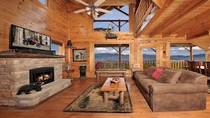 A wooden cabin interior with a fireplace, a television, a sofa, and a view of mountains. - Romantic Escape with panoramic Mountain Views, great location 2.5 steps to enter (Sevierville)