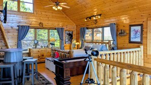 A log cabin interior with a bed, a desk, a chair, a telescope, and a window with a view of trees. - Romantic Escape with panoramic Mountain Views, great location 2.5 steps to enter (Sevierville)