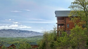 Une cabane en rondins dotée d’un balcon, entourée d’arbres et avec des montagnes en arrière-plan.