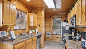 Une cuisine rustique, située dans une cabane en bois, avec des comptoirs en granit, des appareils électroménagers en acier inoxydable et une fenêtre équipée de stores.