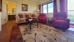Una sala de estar con sofá, dos sillones, una mesita de centro y un amplio ventanal con cortinas.