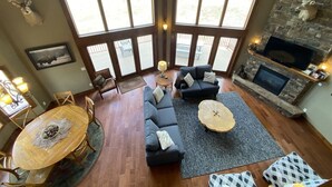 Un salon spacieux doté d’une cheminée en pierre, de grandes fenêtres, d’un coin repas et d’un espace salon confortable.