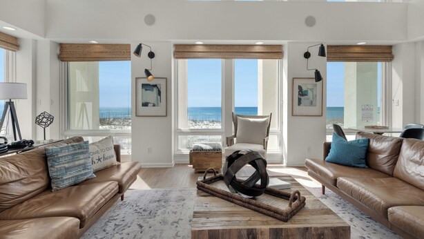 A spacious living room with large windows, a leather sofa, a coffee table, and a view of the beach.