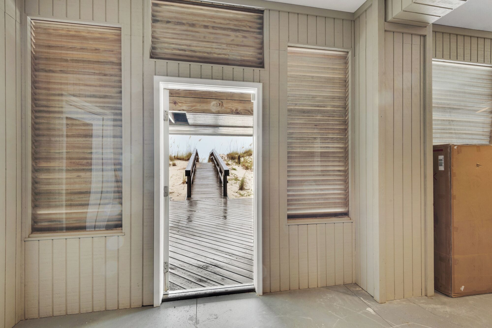 Una porta che dà su una vista mare, con un pontile in legno e un sentiero sabbioso.