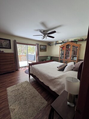 Ein Schlafzimmer mit einem Bett, einem Deckenventilator, einer Holzkommode, einem Schrank und Blick ins Freie.