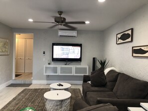 Una sala moderna con ventilador de techo, televisor de pantalla plana, mueble blanco para equipo de entretenimiento, sofá marrón y una pequeña mesa redonda.