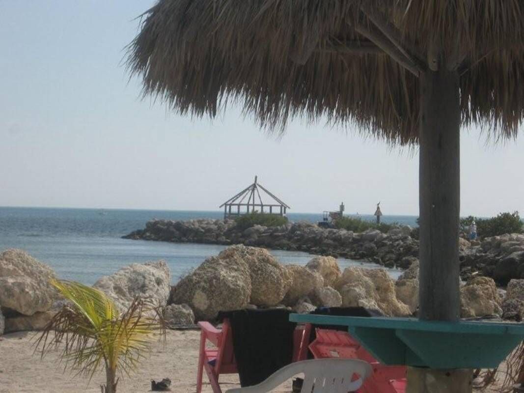 A beach scene with a thatched umbrella, a wooden structure, and rocks in the water.