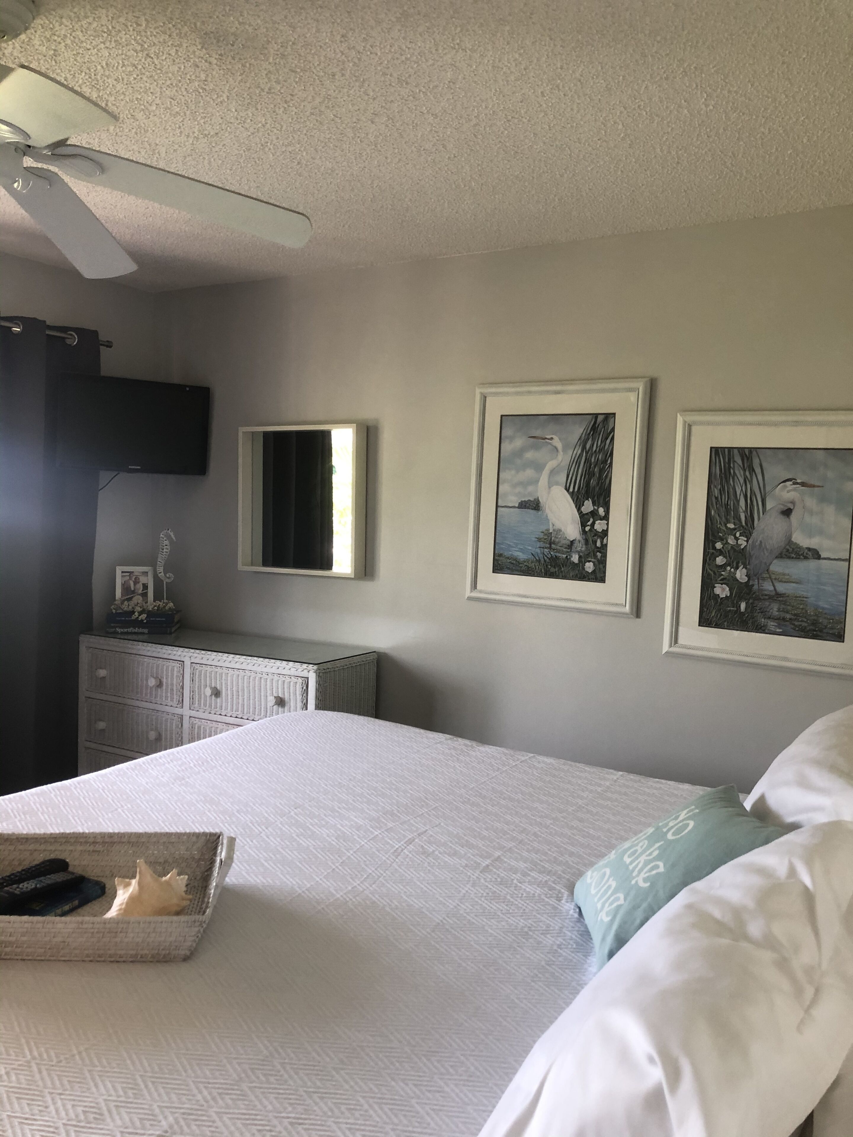 Une chambre à coucher comprenant un lit, une commode, un téléviseur et deux tableaux encadrés accrochés au mur.