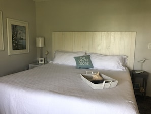 Una cama bien hecha con una almohada que dice "No Wake Zone", una mesita de noche con una lámpara, y un cuadro en la pared.