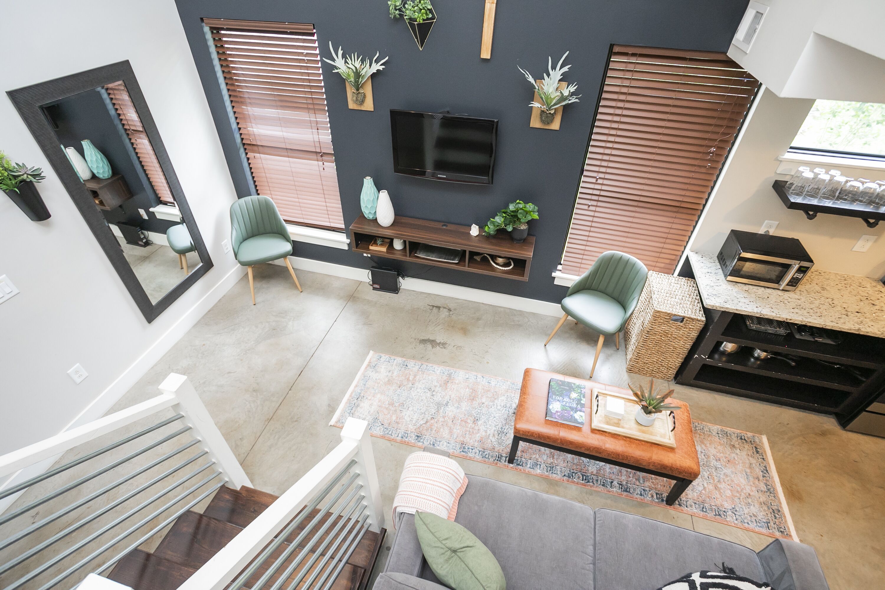 Un salon moderne avec un téléviseur à écran plat, deux fauteuils verts, un canapé gris, une table basse en bois et une petite table d’appoint.