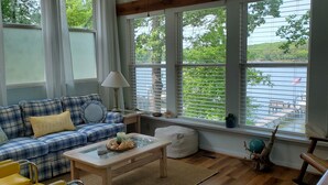A cozy room with a plaid sofa, a small table, and a view of a lake through large windows. - Waterfront with Private Pier and Tranquil Water views! (Gloucester Courthouse)