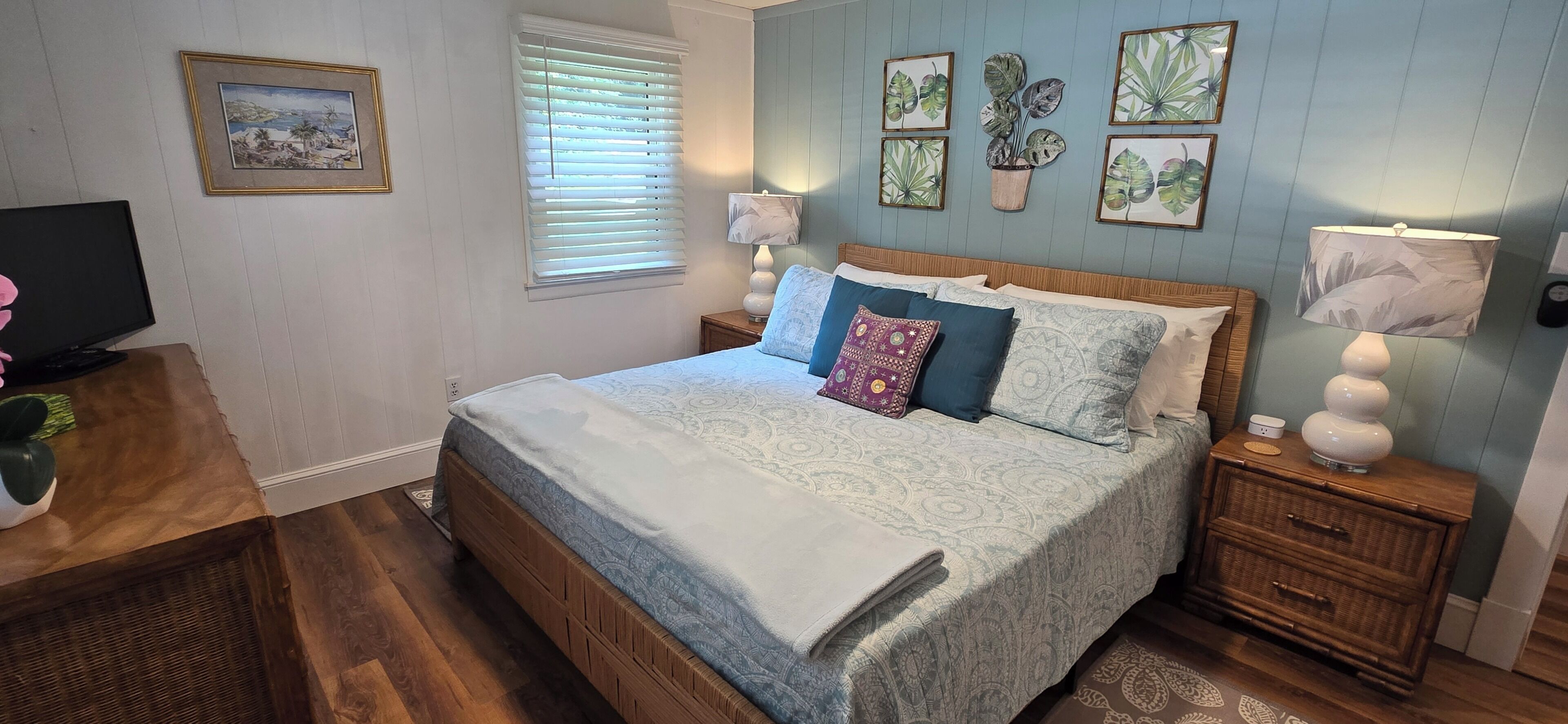 A bedroom with a bed, bedside tables, a television, and wall art.