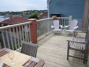 Enjoy a serene view of the water from this deck, featuring a table and two Adirondack chairs.