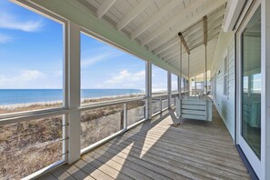 Eine überdachte Holzterrasse mit großen Fenstern mit Blick auf einen Strand.