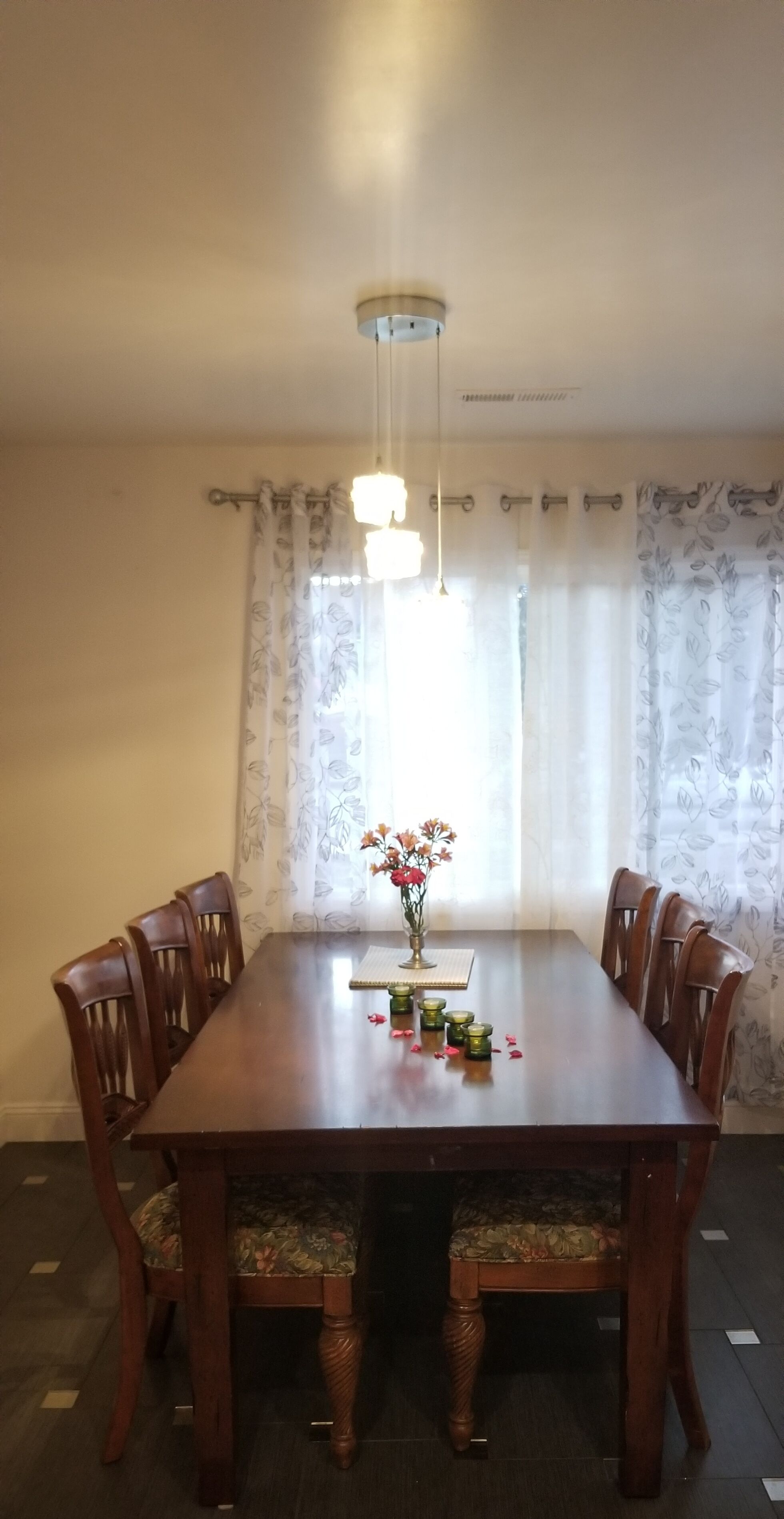 Ein Esszimmer mit Holztisch, sechs Stühlen, einer Blumenvase und einer Deckenleuchte.