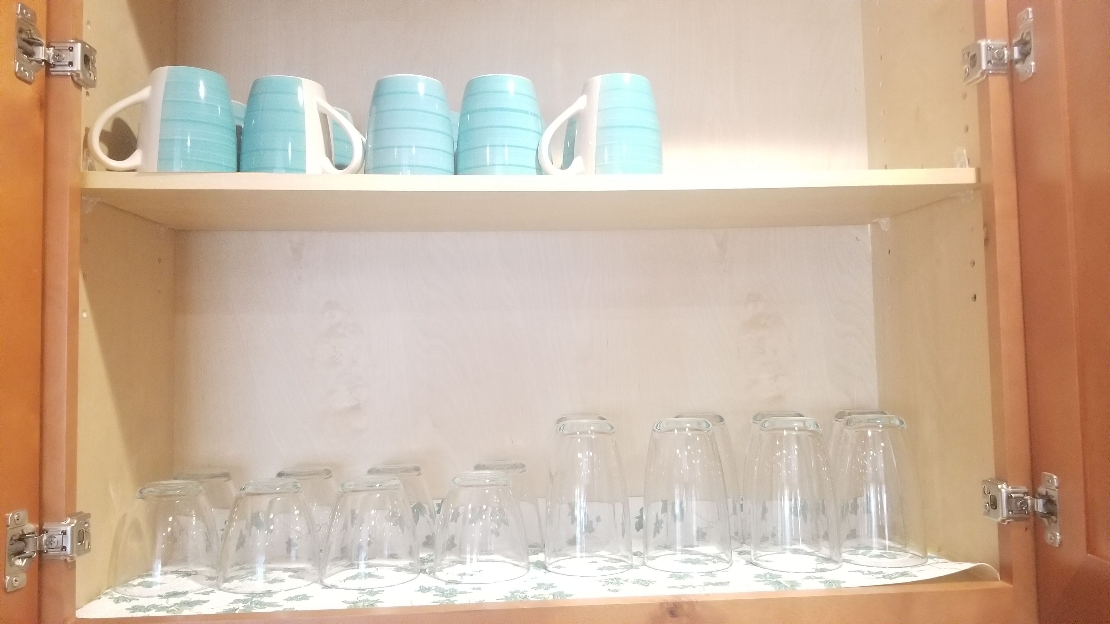 Un mueble de madera con estantes que contienen tazas azules y botellas de vidrio transparente.