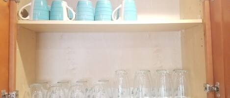 Un mueble de madera con estantes que contienen tazas azules y botellas de vidrio transparente.