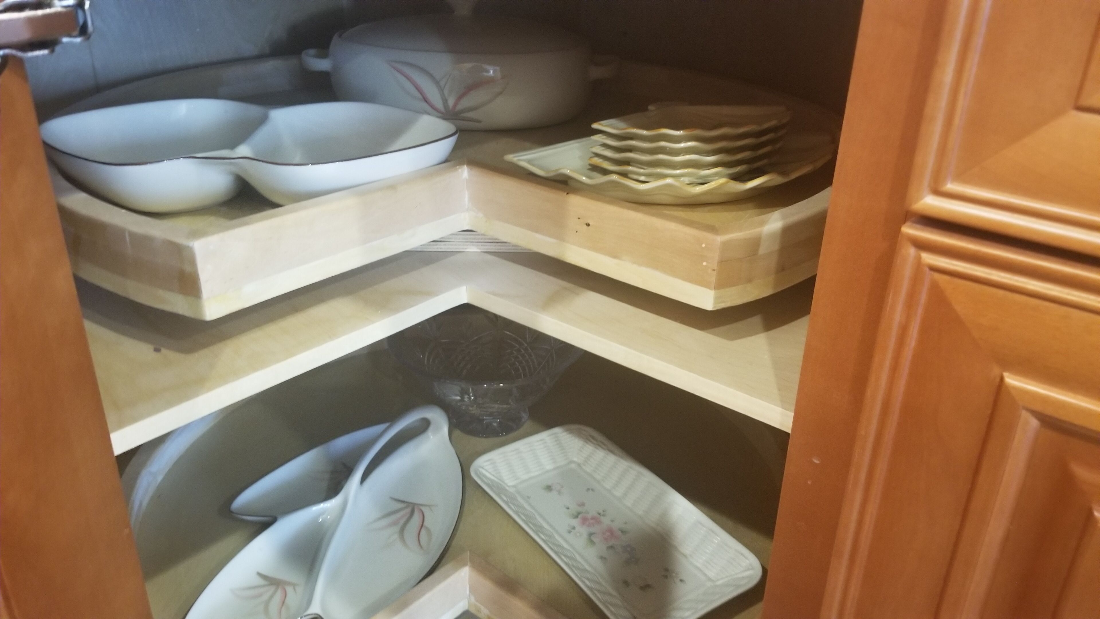 Et køkken med hvide og beige skabe, en mikrobølgeovn samt diverse tallerkener og skåle på hylder.
