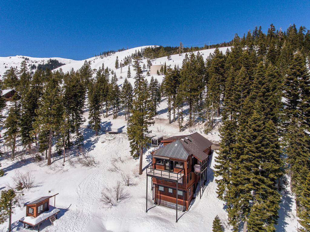 Une cabane en bois dotée d’un balcon, entourée de neige et de pins, située dans une région montagneuse.