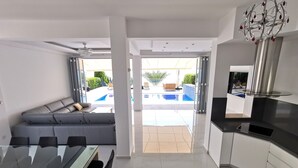 Una cucina moderna con zona pranzo, un ampio divano grigio e vista su una piscina.