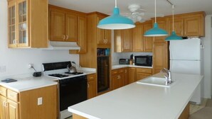 A kitchen with wooden cabinets, a white countertop, a stove, a microwave, and a refrigerator. - Quiet North Beach Oceanfront Steps to Private Beach  3 Night Min Stays Available (North Beach)
