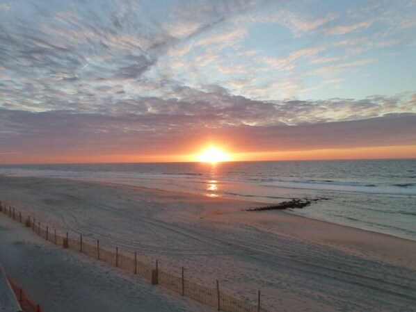 Une plage bordée d’une clôture et où le soleil se couche sur l’oc éan.