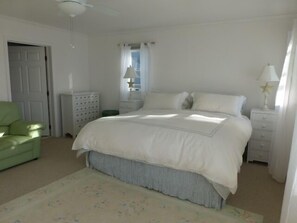 Une chambre à coucher comprenant un lit, une table de chevet, une commode, une chaise et une fenêtre avec des rideaux.