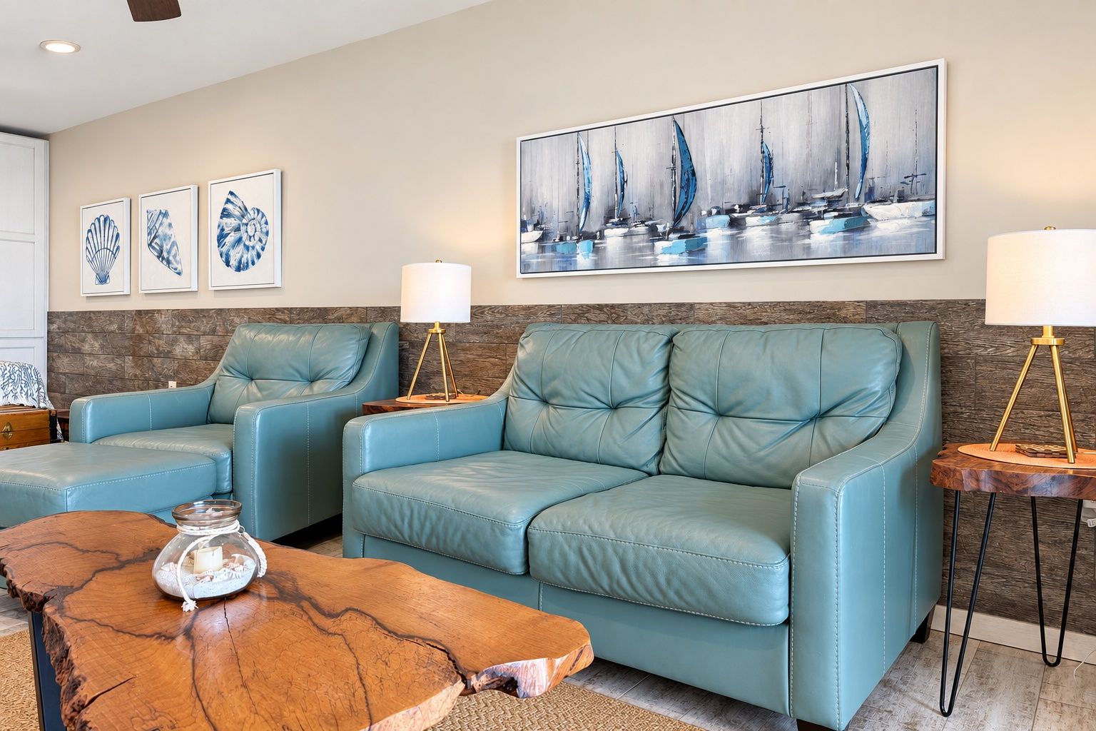 A living room with a blue leather sofa set, a wooden coffee table, and a wall-mounted painting of sailboats.