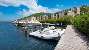 A marina with boats docked, a wooden pier, and a building with balconies. - Our Walk in Paradise Level at Sapphire Village, East End (St Thomas)