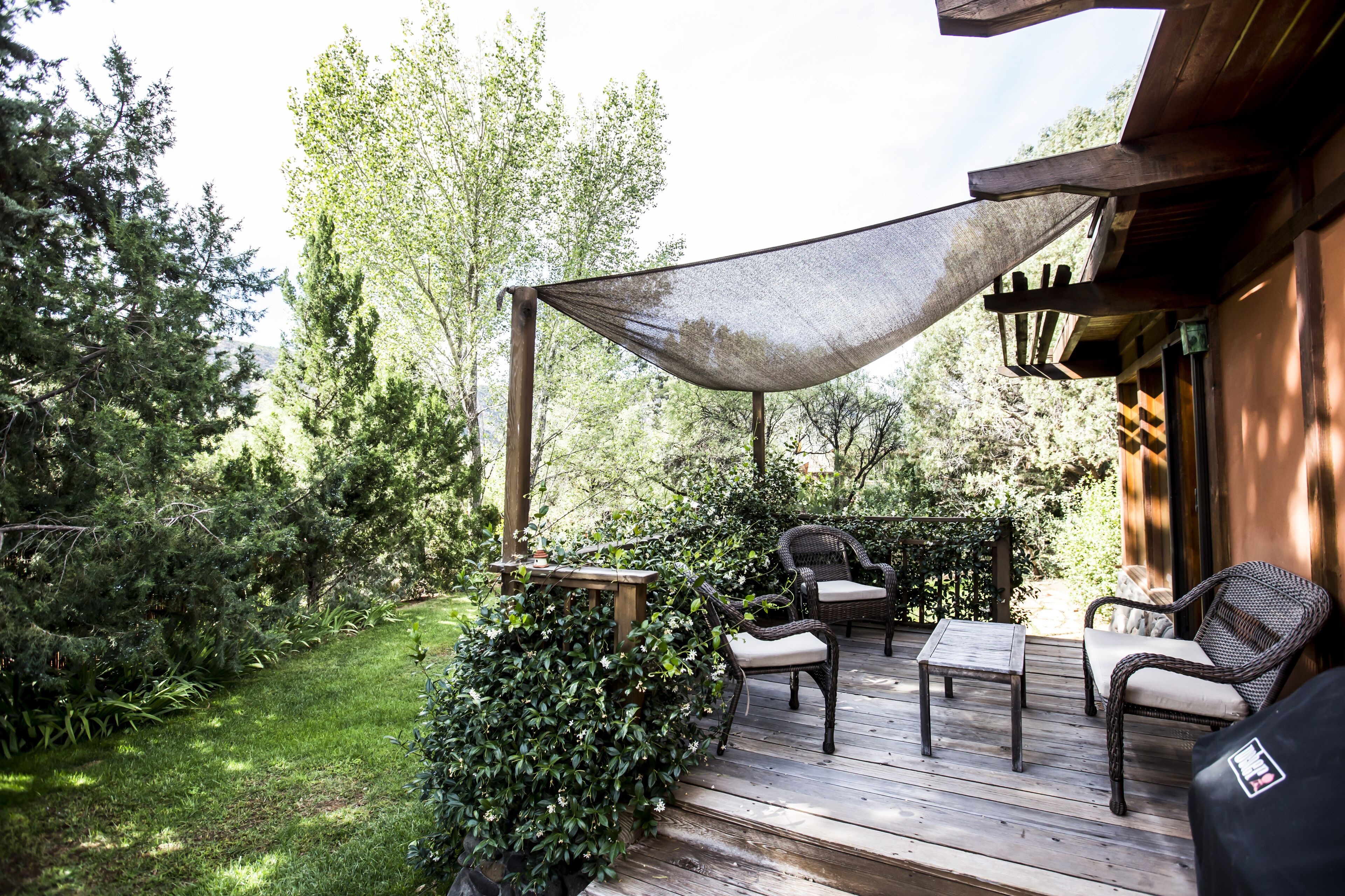 A wooden deck with outdoor furniture, including chairs and a table, surrounded by greenery.
