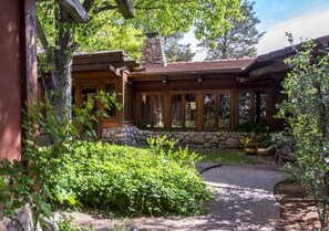Un chalet rustique doté d’une cheminée en pierre, de grandes fenêtres et d’un jardin bien entretenu.