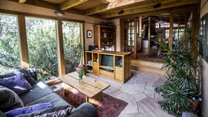 A cozy living room with a sofa, coffee table, wooden entertainment unit, and large windows overlooking a forest. - Oasis Retreat Nestled Near World Renown Hiking (Sedona)