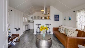 Een moderne woonkamer met een bruine bank, een ronde salontafel met een bloevas, en een keuken op de achtergrond.