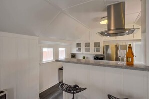 Uma cozinha moderna com armários brancos, coifa de aço inoxidável e um espaço bar com banquetas.