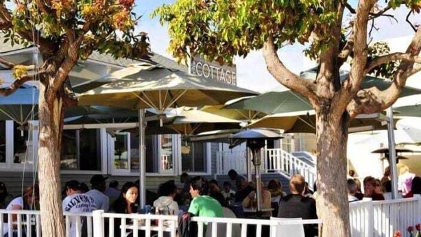 A restaurant with outdoor seating, umbrellas, and a white fence.
