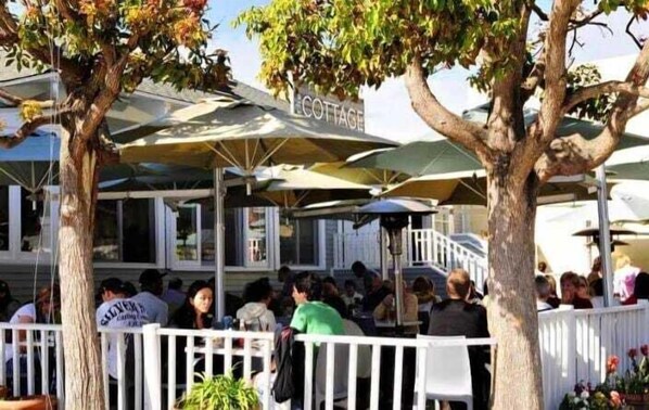 A restaurant with outdoor seating, umbrellas, and a white fence.