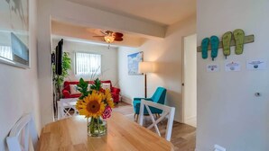 A dining area with a wooden table, a vase of sunflowers, and a view into a living room with a red sofa and blue chairs.