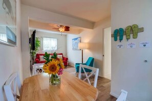 A dining area with a wooden table, a vase of sunflowers, and a view into a living room with a red sofa and blue chairs.