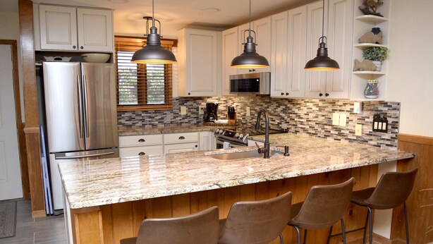 A modern kitchen with a large island, bar stools, stainless steel appliances, and pendant lighting.